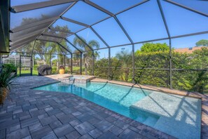 Relax by the pool surrounded by lush greenery and a clear sky.
