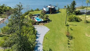 A modern house with a pool, surrounded by a grassy area and a lake. - A Luxury Bayfront Retreat with a Resort-Style Pool & Private Dock (Panama City)