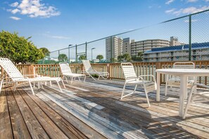 A wooden deck with white lounge chairs and a table, surrounded by a chain-link fence. - 🌊Gulf Front with Gorgeous Views | Seaside Beach & Racquet Club 1315🌊 (Orange Beach)