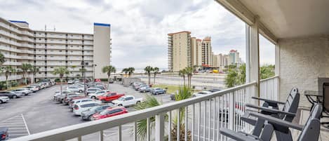 A balcony with a view of a parking lot, palm trees, and high-rise buildings in the background.