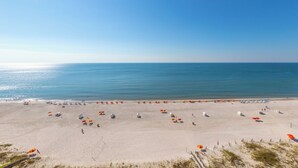 Une vaste plage de sable, parsemée de parasols et de chaises longues, un ciel bleu azur et l’océan en toile de fond.