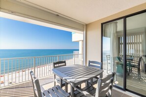 En balkon med et bord og stole, der ud til en strand og havet.