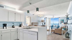 A modern kitchen with white cabinets, a dishwasher, and a dining area with a view of the ocean. - 🌊Shoalwater 903 | Gulf Front | Breathtaking Views🌊 (Orange Beach)