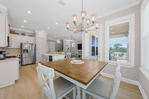 A modern kitchen with white cabinets, a stainless steel refrigerator, a wooden dining table, and a chandelier. - ⭐Fabulous Amenities | Close to Beach | Summer Salt 24181⭐ (Orange Beach)