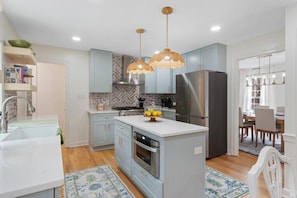 Una cocina moderna con armarios azul claro, una isla central, electrodomésticos de acero inoxidable y lámparas colgantes.