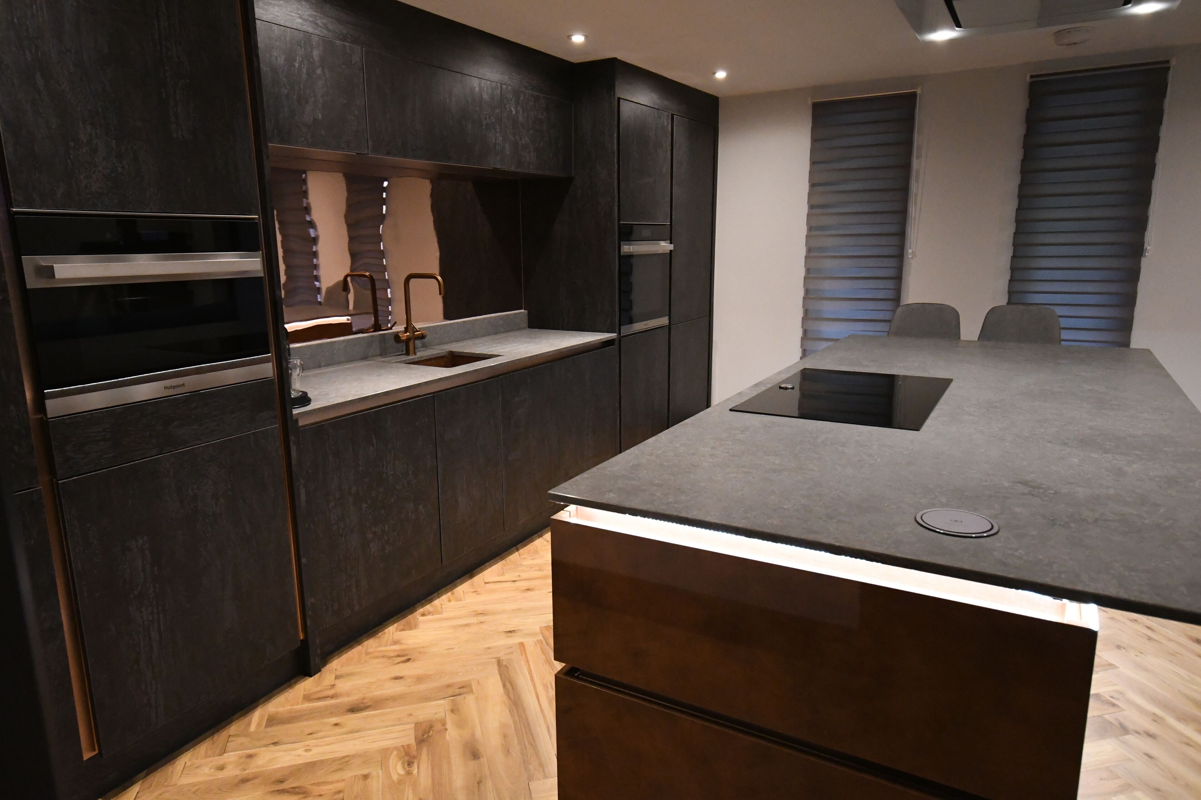 A modern kitchen with dark cabinetry, a central island, and a built-in oven.