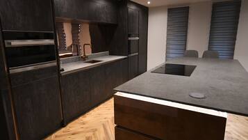 A modern kitchen with dark cabinetry, a central island, and a built-in oven.