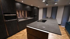 A modern kitchen with dark cabinetry, a central island, and a herringbone wood floor. - Luxury 2 bedroom-Fully Accessible ground floor property. Norfolk, Attleborough. (Attleborough)