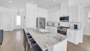 A modern kitchen with white cabinetry, a marble countertop, and stainless steel appliances.