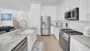 A modern kitchen with white cabinetry, stainless steel appliances, and a marble countertop.