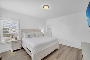 A bedroom with a bed, a nightstand, a window with blinds, and a door.