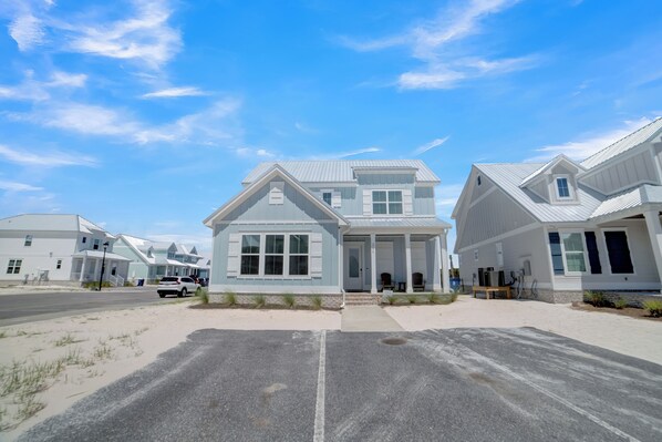 A row of coastal houses with a sandy driveway and a clear blue sky.