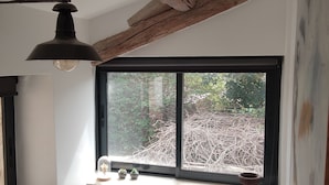 Une pièce dotée d’une grande fenêtre, de poutres apparentes, d’une lampe suspendue et d’une petite table agrémentée d’objets décoratifs.