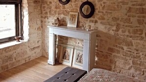 Une pièce rustique aux murs en pierre apparentes, avec un banc en bois, une console blanche agrémentée d’objets décoratifs et une fenêtre offrant une vue agréable.