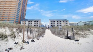 En sandstig som leder till ett hotell vid stranden, med en hög byggnad som syns i bakgrunden.