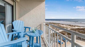 A balcony with blue chairs and a table, overlooking a beach.