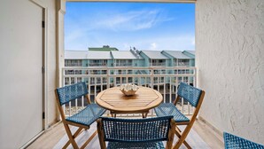En balkon med et rundt træbord og fire blå fletstole, med udsigt over en bygning med flere balkoner.