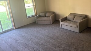 A spacious room with carpeted flooring, two sofas, a ceiling fan, and large windows.