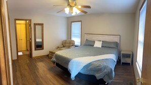 A bedroom with a bed, a chair, a ceiling fan, and a window.