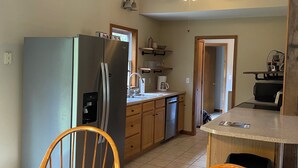 A kitchen with a refrigerator, stove, and wooden chairs around a table.