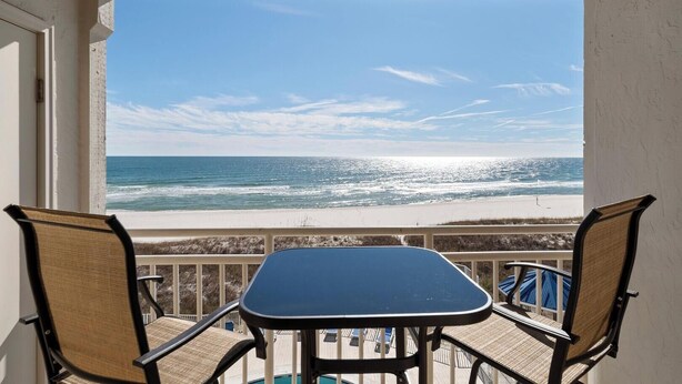 Un balcón con una mesa y dos sillas con vista a la playa.