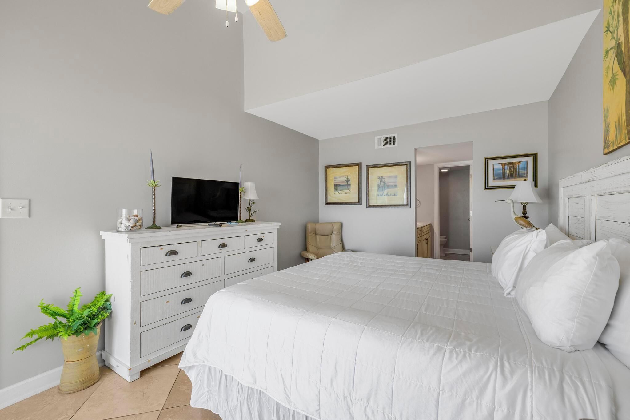 A bedroom with a large bed, a dresser, a television, and framed pictures on the wall.