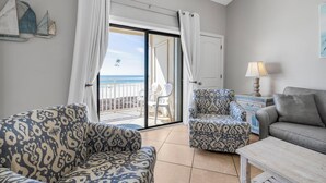 Une pièce avec des canapés à motifs, une petite table et une vue sur la mer, visible à travers une porte coulissante.