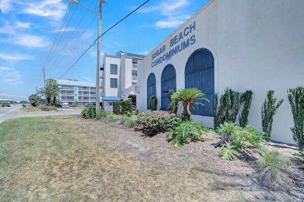 A building with the sign "Sugar Beach Condominiums" and a landscaped garden with various plants.