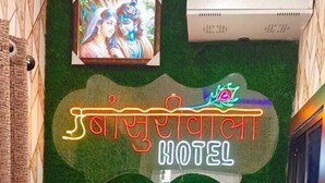 Two individuals in blue shirts standing in a room with a green wall, a neon sign reading "Hotel", and a television mounted on the wall. - hotel basurivala  (Bhopal)