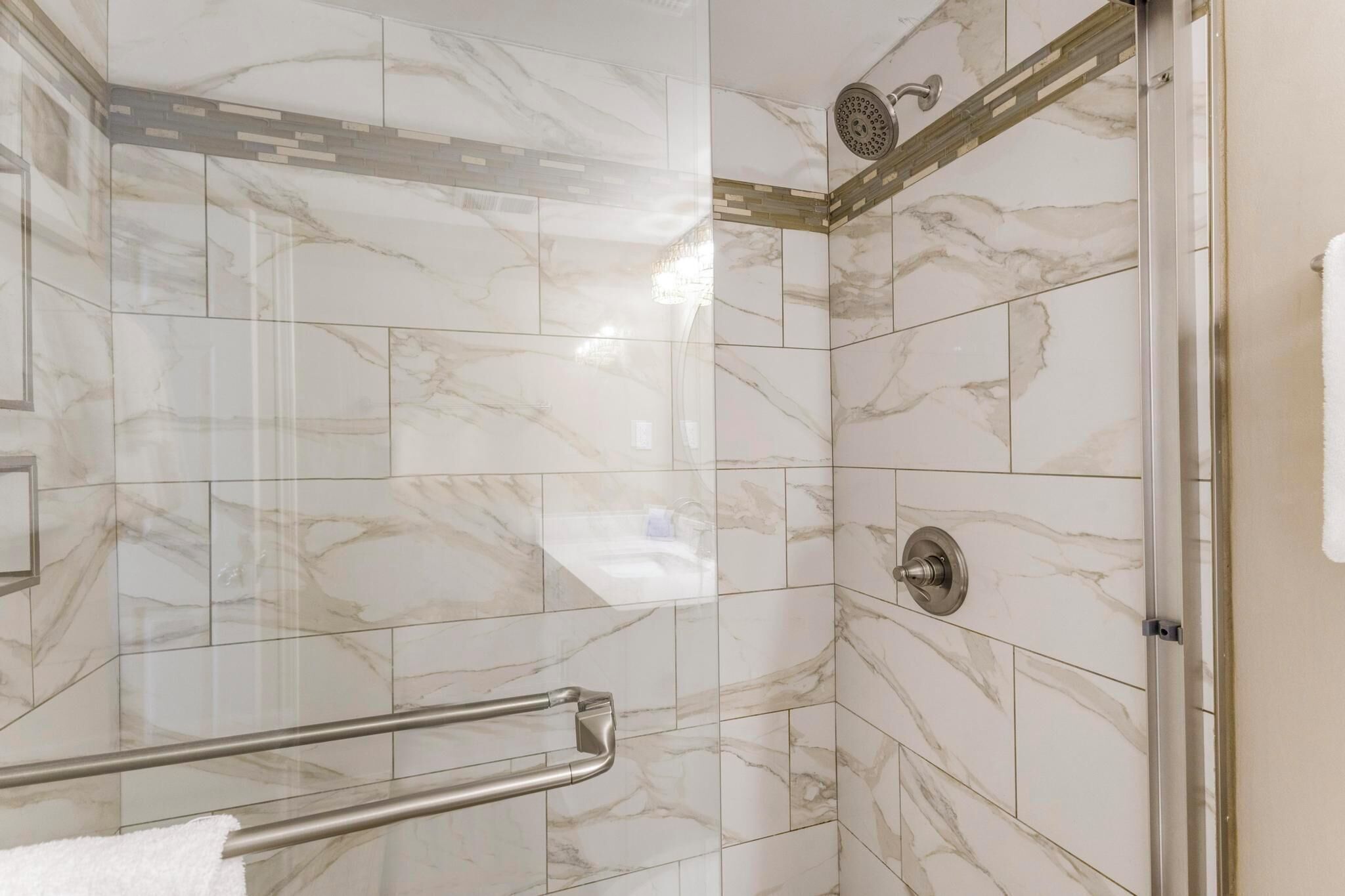 A shower with marble tiles, a handrail, and a towel rack.