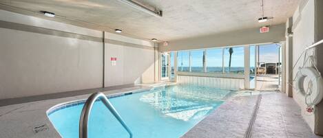 An indoor swimming pool with clear glass walls, a lifebuoy, and an exit sign.