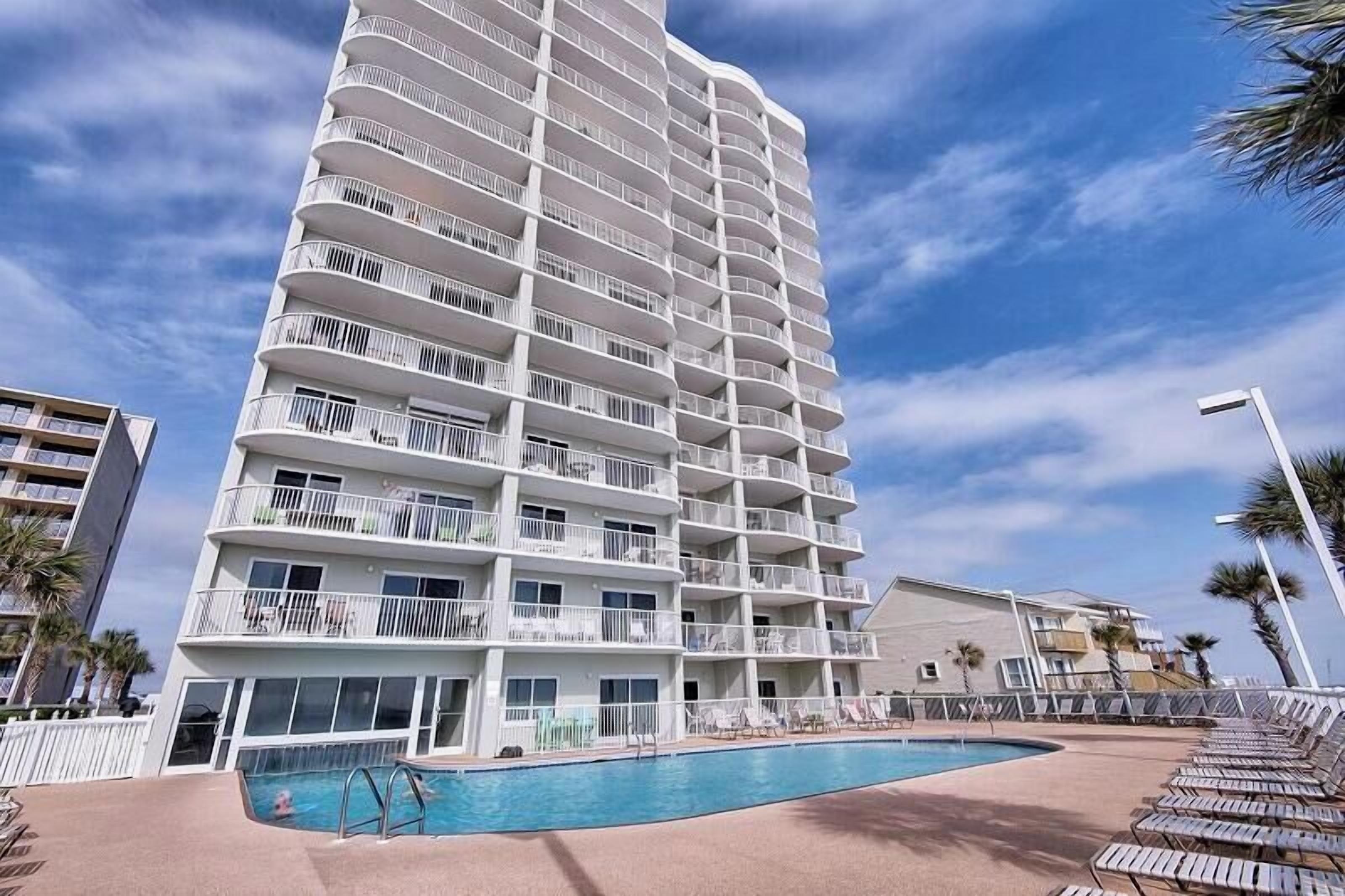 Ein mehrstöckiges Hotel mit Balkonen, einem Schwimmbad und Liegestühlen.