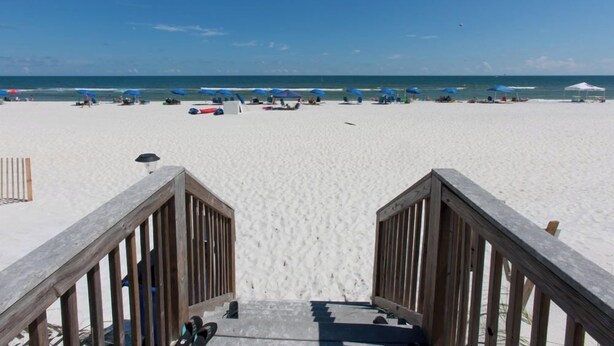 A beach with a wooden walkway leading to the sand, umbrellas, and beach chairs.