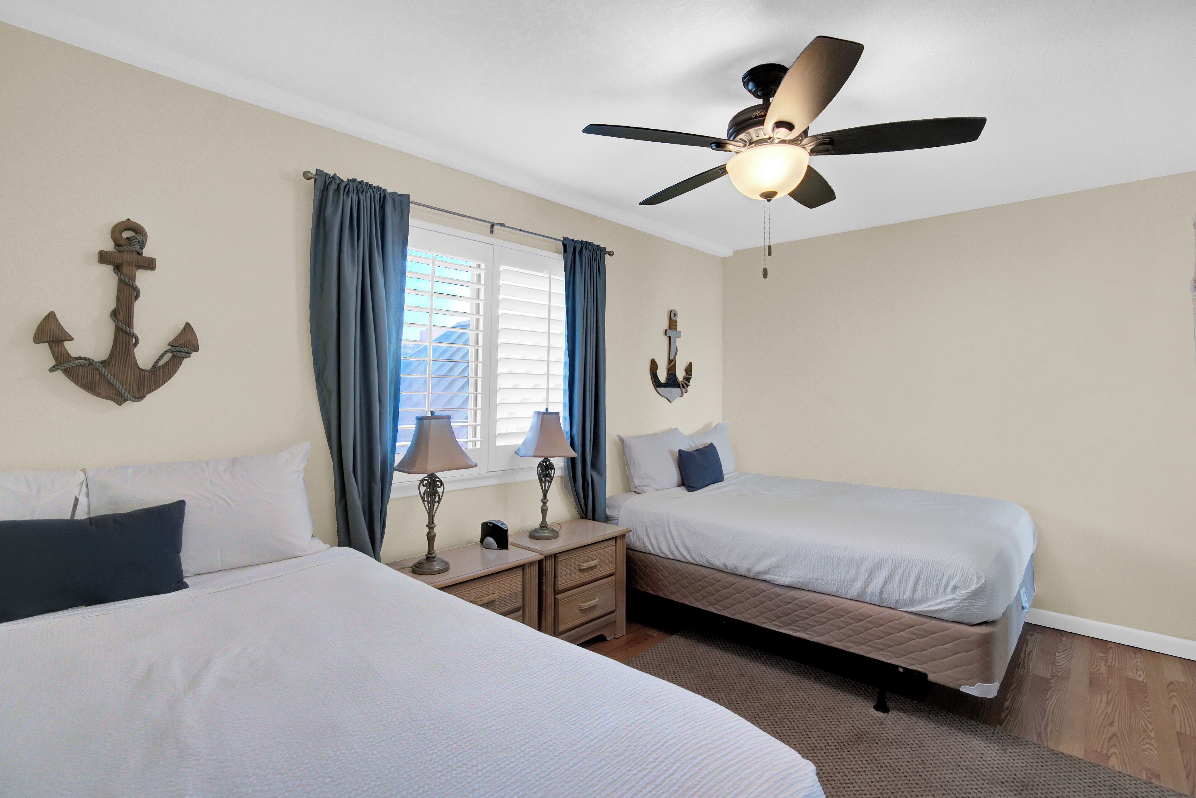 A bedroom with two beds, a ceiling fan, and a window with curtains.