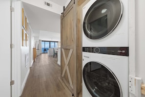 A laundry room with two stacked front-loading washers and dryers, wooden flooring, and a view of the sky through large windows.