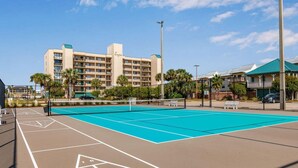 A tennis court with a net, surrounded by a fence, and a building with balconies in the background. - ⭐Wind Drift 702E | Gulf Front with Gorgeous Views | Walk to Beach⭐ (Orange Beach)