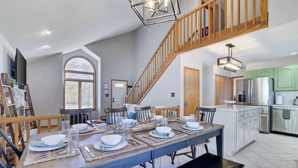 A dining area with a long table set for six, a staircase, and a kitchen with modern appliances.