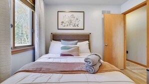 A neatly made bed with a headboard, a framed floral artwork above it, and a wooden door to the right.