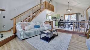 A spacious living area with a wooden staircase, a sofa, a coffee table, and a kitchen in the background.