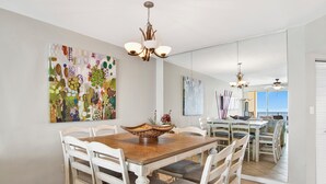 A dining area with a wooden table and white chairs, a chandelier, and abstract art on the walls. - 🌊Windward Pointe 1002 | Gulf Front | Awesome Amenities🌊 (Orange Beach)