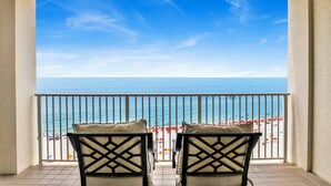 A balcony with two chairs facing a beach with umbrellas and people. - 🌊Windward Pointe 1002 | Gulf Front | Awesome Amenities🌊 (Orange Beach)