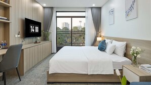 A modern hotel room with a large bed, a desk, a TV, and a balcony with a city view. - Cosmos Hotel Apartment (Hanoi)