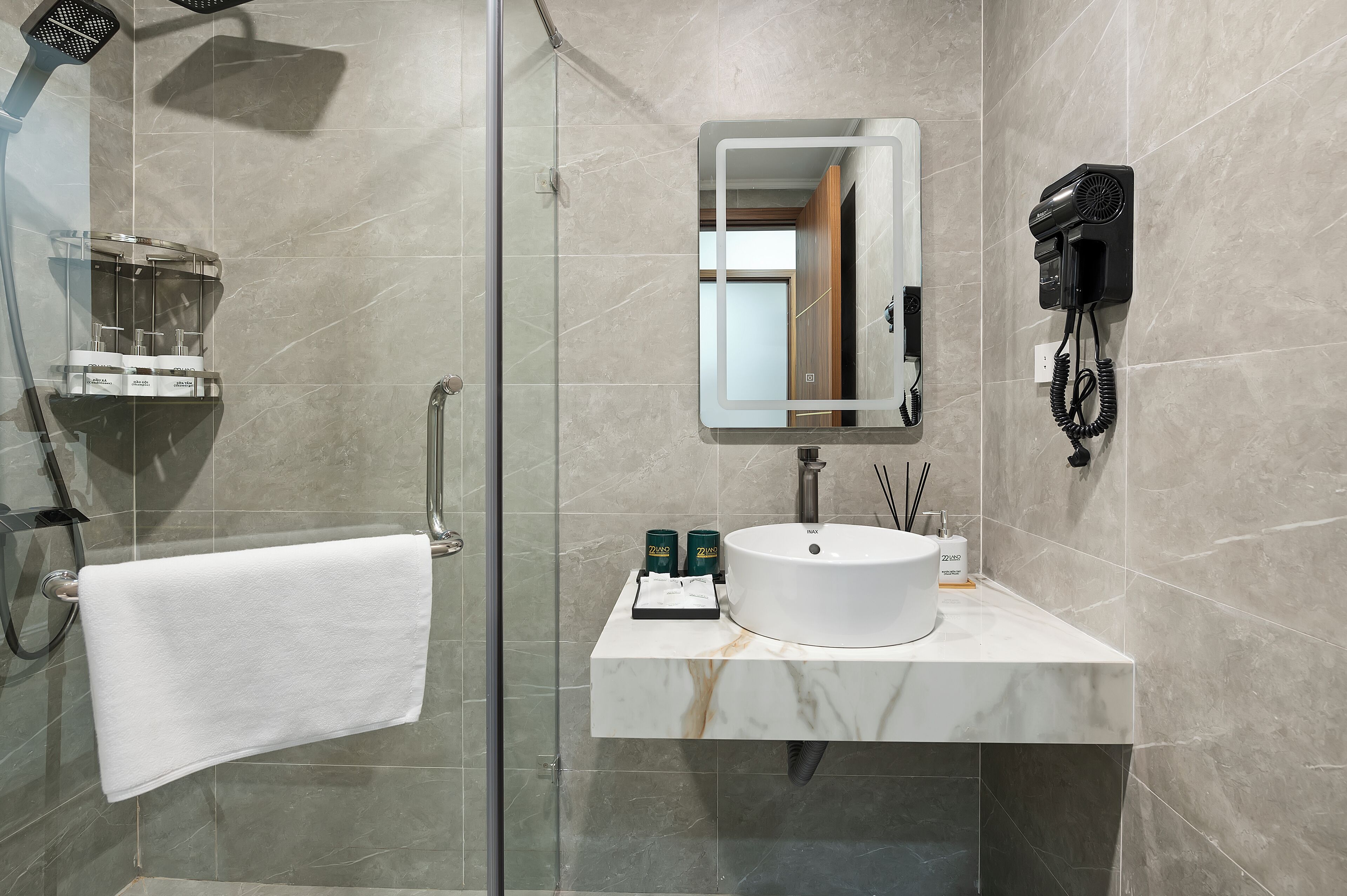 A modern bathroom with a glass-enclosed shower, a white sink, and a mounted hairdryer.