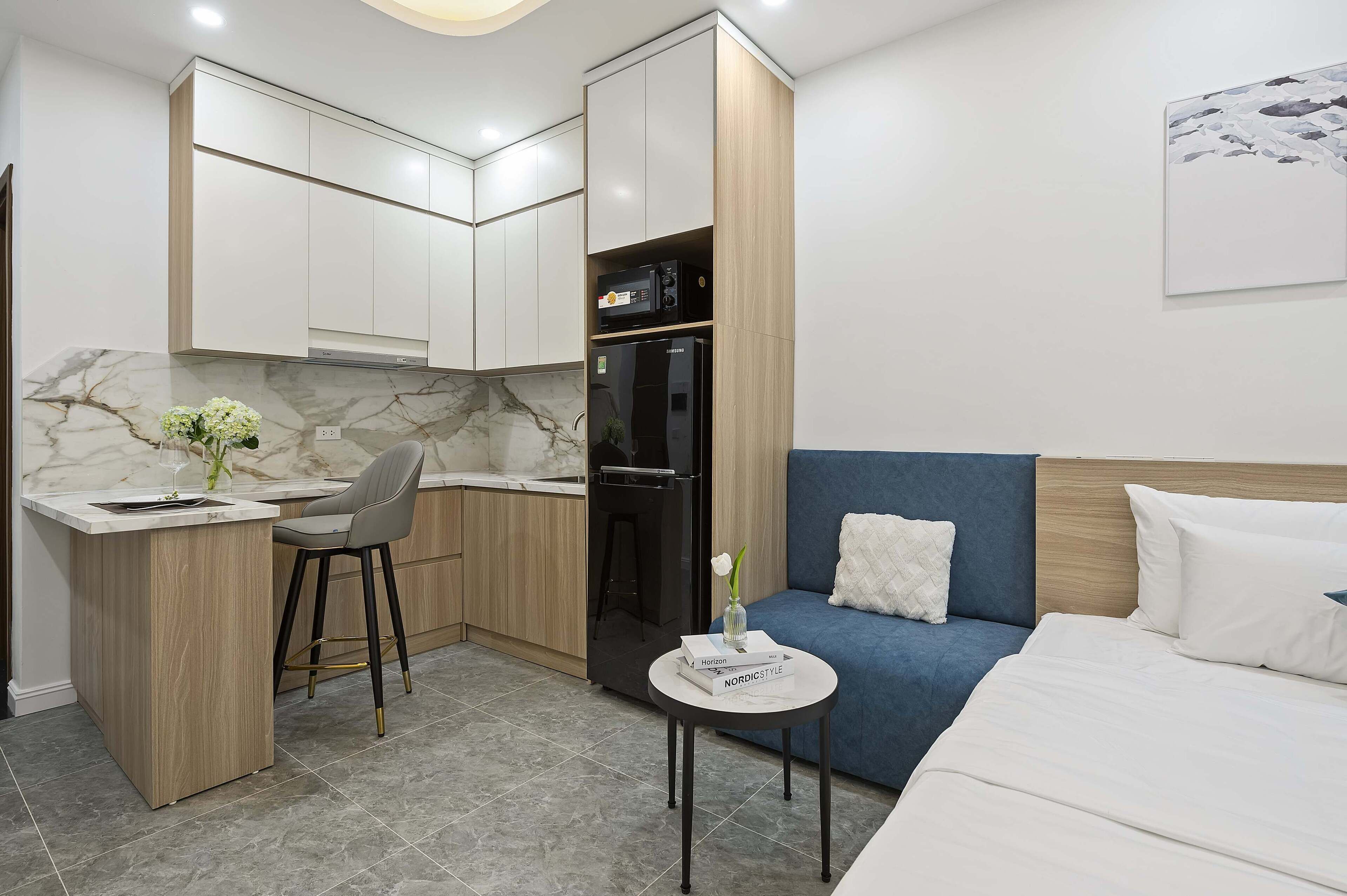 A compact hotel room with a kitchenette, a bed, a small round table, and a blue sofa.