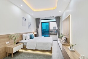 Une chambre d’hôtel moderne avec un grand lit, une table de chevet et une vue sur la ville, visible à travers une porte vitrée.