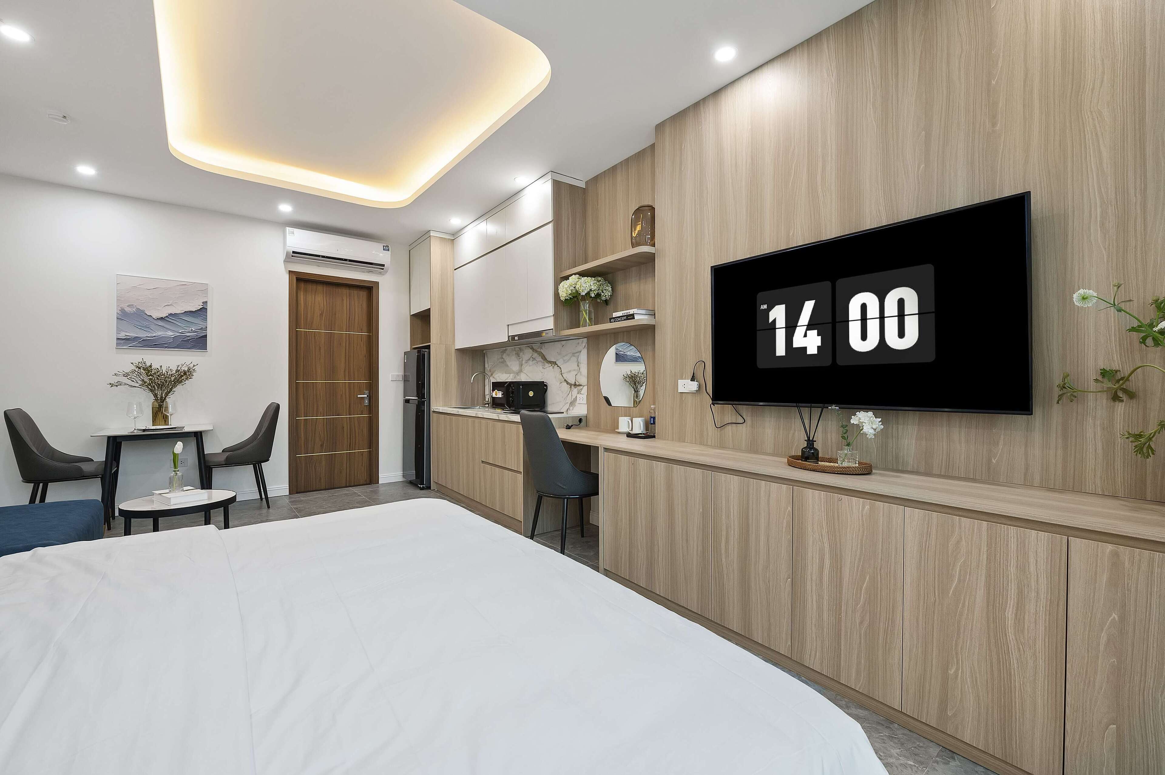 A modern hotel room with a large bed, a desk with a chair, a small table with two chairs, a TV mounted on the wall, and a wooden panel design.