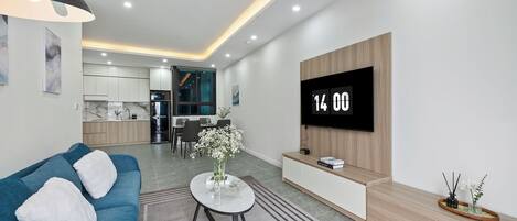 Una sala de estar moderna con sofá, una mesa de centro, un televisor montado en la pared y una cocina al fondo.