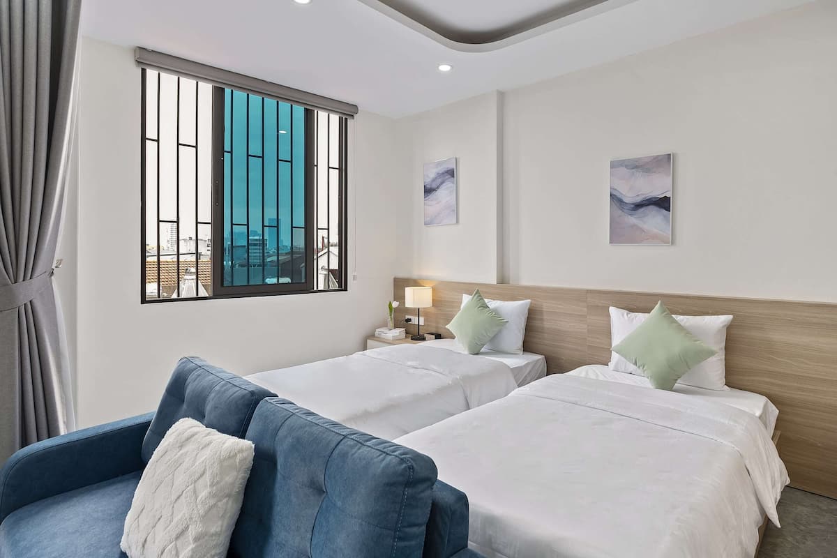 A hotel room with two beds, a blue sofa, a window with bars, and artwork on the walls.