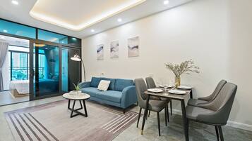 A modern living room with a blue sofa, a dining table with chairs, and a large window with a view of buildings.