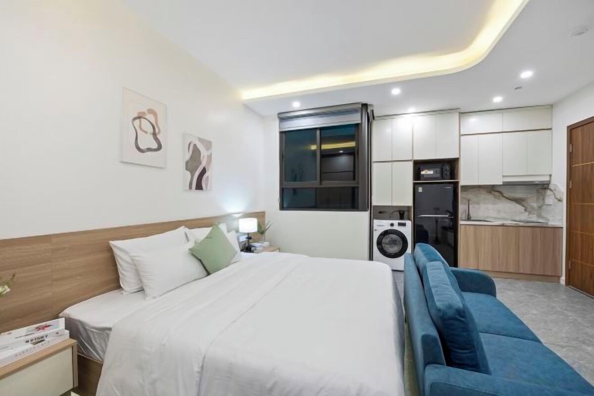 A modern hotel room with a bed, a sofa, a desk, and a washing machine.